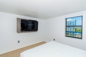 Ein schlicht eingerichtetes Schlafzimmer mit großem Fenster, einem Bett und einem Wand-Fernseher.