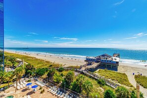Ein Strandhotel mit Promenadenweg zum Strand, einem Poolbereich und einem Rettungsschwimmturm.