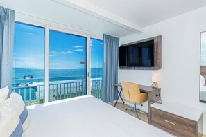 A hotel room with a large bed, a desk, a chair, a TV mounted on the wall, and a balcony with a view of the sea. - Myrtle Beach Oceanfront Retreat 2 BR Condo Yachtsman S706 (Myrtle Beach)
