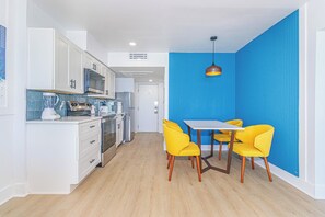 A compact kitchen with white cabinets, a microwave, and a stove. There is a dining area with a table and four yellow chairs. - Myrtle Beach Oceanfront Retreat 2 BR Condo Yachtsman S706 (Myrtle Beach)