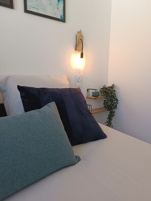 A bed with pillows, a wall-mounted light, a power outlet, and a small shelf with a plant. - Studio 'Le Cocoon des Rives' at the gates of Roanne (Commelle-Vernay)