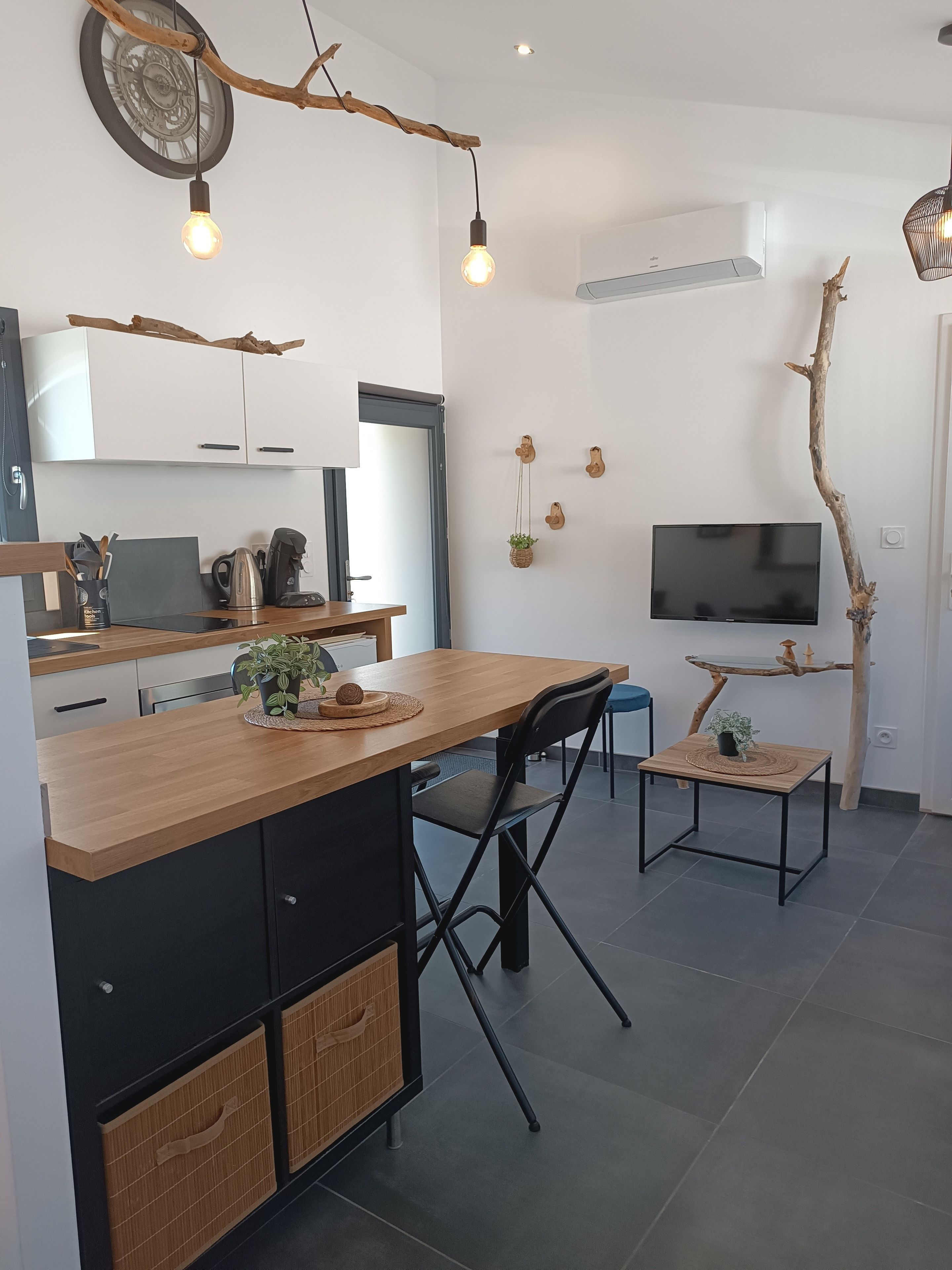Une cuisine moderne avec un îlot central en bois, des meubles de couleur noire et un téléviseur encastré.