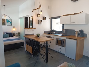 A compact kitchen with a dining area, a bed, and a large window. - Studio 'Le Cocoon des Rives' at the gates of Roanne (Commelle-Vernay)