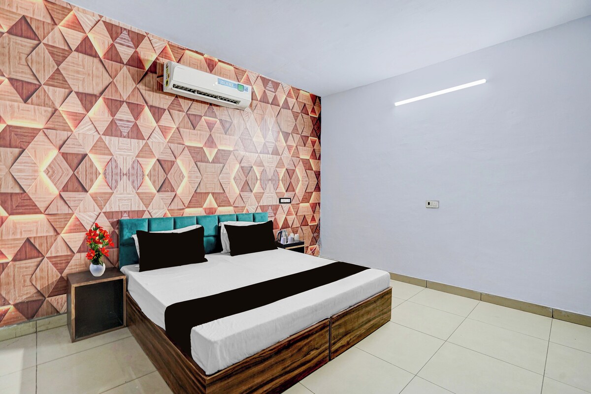 Una habitación de hotel con un muro de diseño geométrico, una cama con cabecera de madera y un equipo de aire acondicionado sobre la cama.