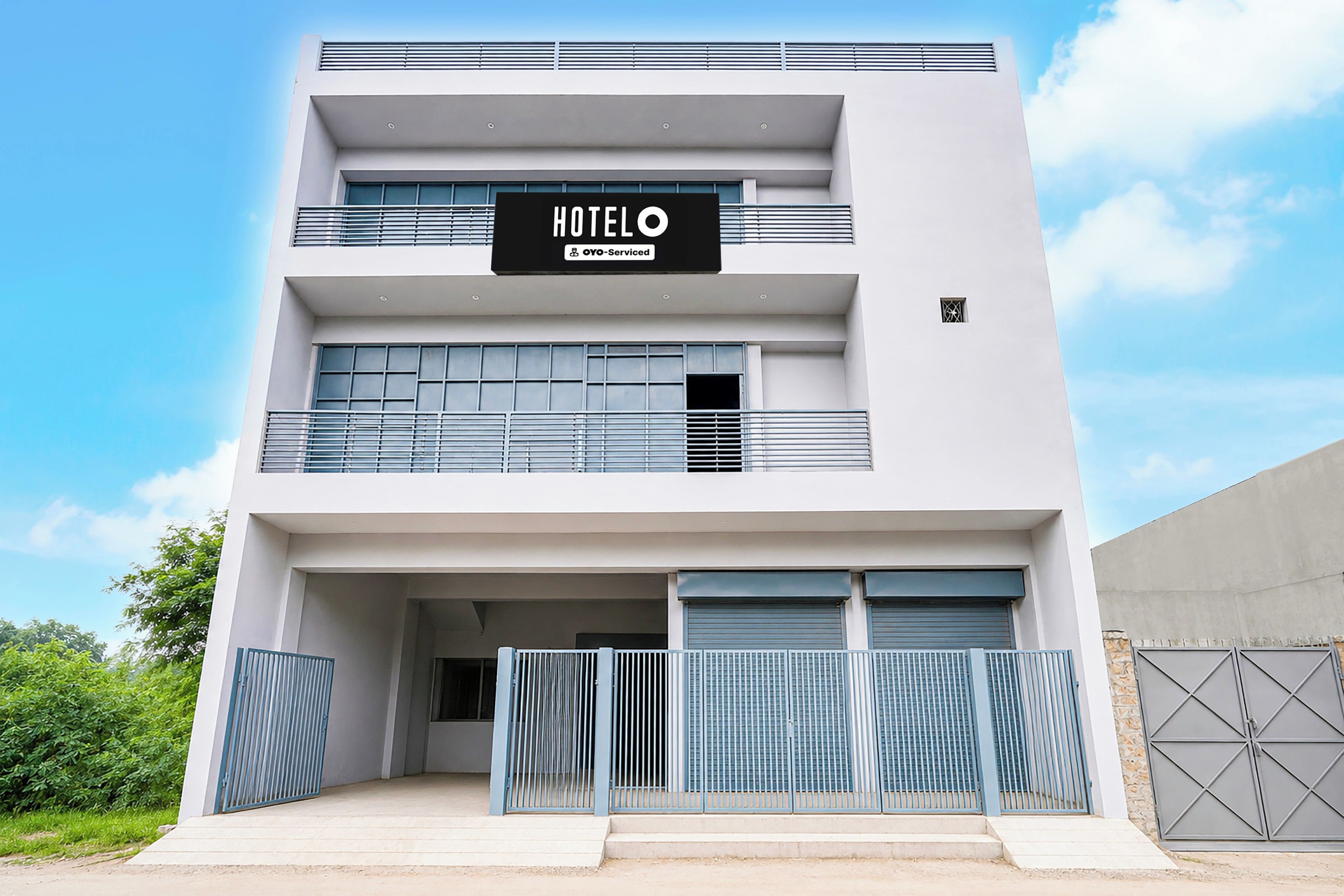 A modern hotel building with a sign reading 'HOTEL OYO-Serviced' and a gated entrance.