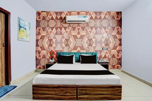 A bedroom with a geometric patterned wall, a bed with black and white bedding, a teal headboard, a nightstand with a lamp, and a potted plant.