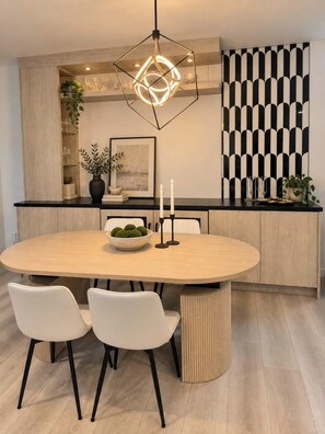 Une cuisine moderne avec une table à manger ronde, des chaises blanches, un luminaire suspendu aux motifs géométriques et un mur aux motifs noir et blanc.