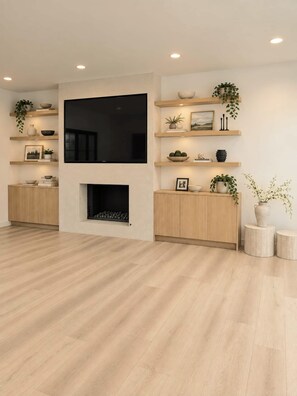 Ein modernes Wohnzimmer mit Flachbildfernseher an der Wand, Holzboden, eingebauten Regalen mit Dekoration und einem Kamin.