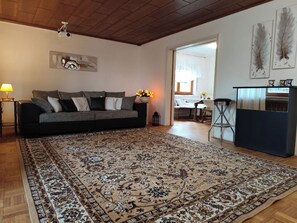 A living room with a large patterned rug, a sofa, a coffee table, and a TV mounted on the wall. - Großes Haus in Sandweier für bis zu 16 Gäste – 8 Schlafzimmer (Baden-Baden)