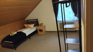 A small, cozy room with a sloped ceiling, a single bed with a nightstand, a radiator, and a window with curtains. - Großes Haus in Sandweier für bis zu 16 Gäste – 8 Schlafzimmer (Baden-Baden)