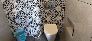 A bathroom with patterned tiles, a toilet, and a blue bucket. - Eco-friendly 2-bedroom house with mountain view in charming Thenkarai with AC (Thenkarai)