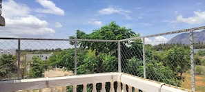 A balcony with a chain-link fence, overlooking a residential area with trees and a mountain in the background. - Eco-friendly 2-bedroom house with mountain view in charming Thenkarai with AC (Thenkarai)