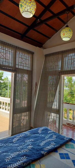 A room with a bed, a ceiling fan, and a view of greenery outside. - Eco-friendly 2-bedroom house with mountain view in charming Thenkarai with AC (Thenkarai)