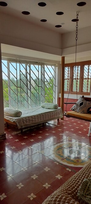 A room with a bed, a hanging swing, and large windows with a view of greenery. - Eco-friendly 2-bedroom house with mountain view in charming Thenkarai with AC (Thenkarai)