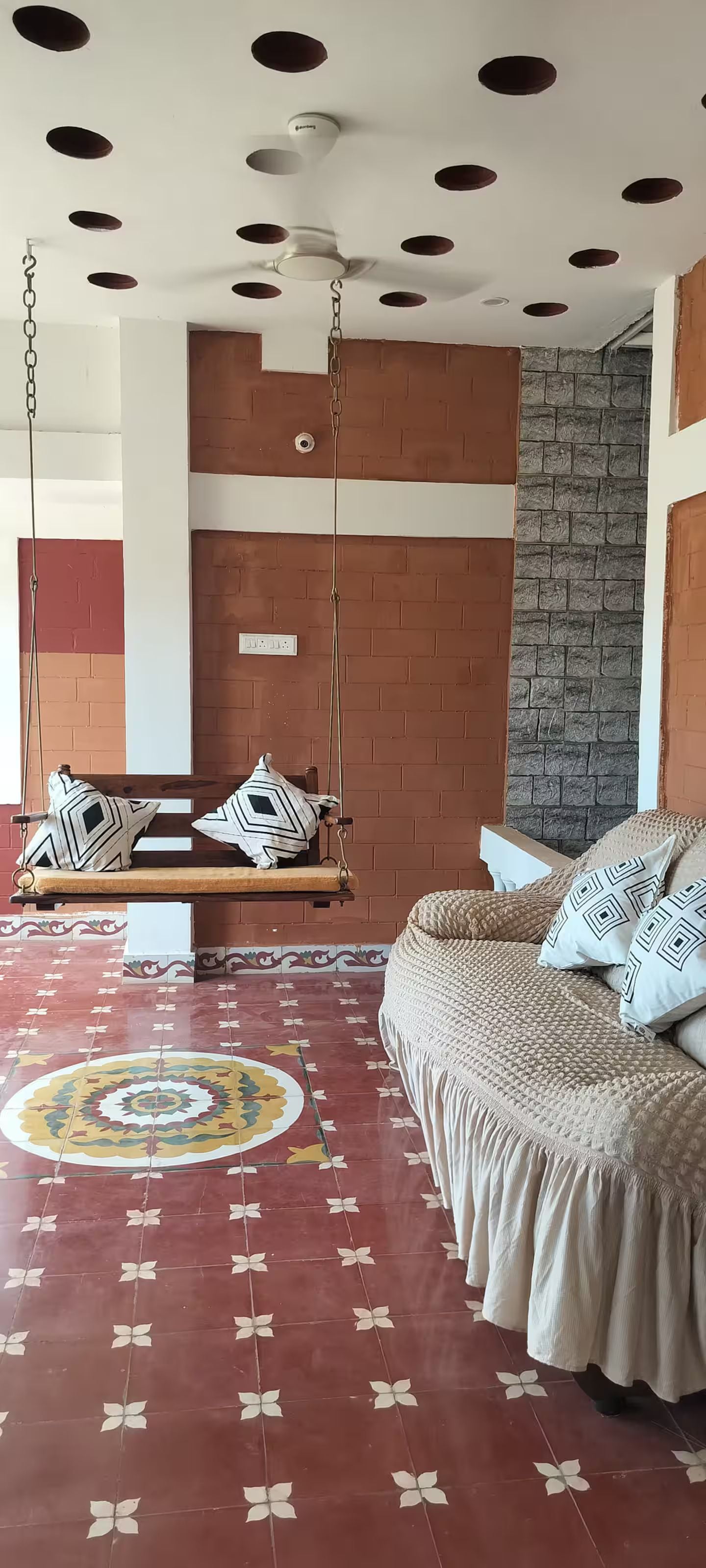 A room with a bed, a swing, a patterned floor, and a brick wall.