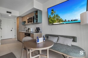 A modern kitchen with a dining area, a flat-screen TV displaying a tropical beach scene, and a seating area with a cushioned bench. - Luxury Studio in Miami -46th Floor, Pool (Miami)