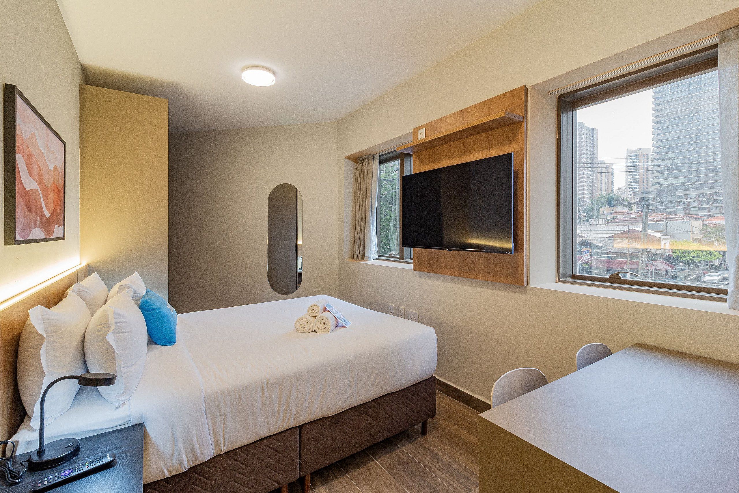 A hotel room with a bed, a desk, a television, and a window with a city view.