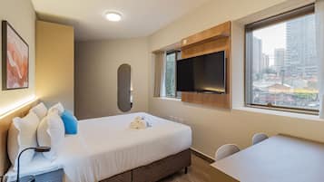 A hotel room with a bed, a desk, a television, and a window with a city view.