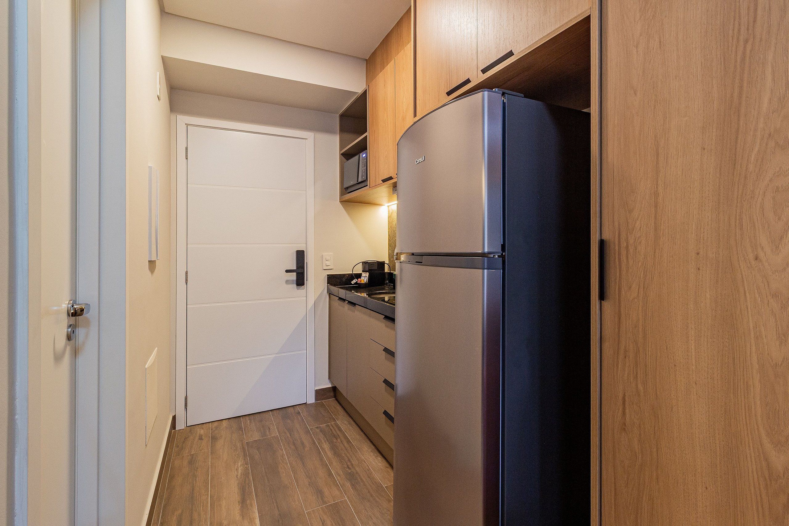 A compact kitchen with a built-in refrigerator, wooden cabinets, and a microwave on the countertop.
