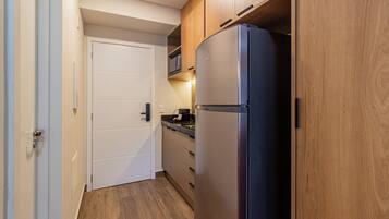 A compact kitchen with a built-in refrigerator, wooden cabinets, and a microwave on the countertop.