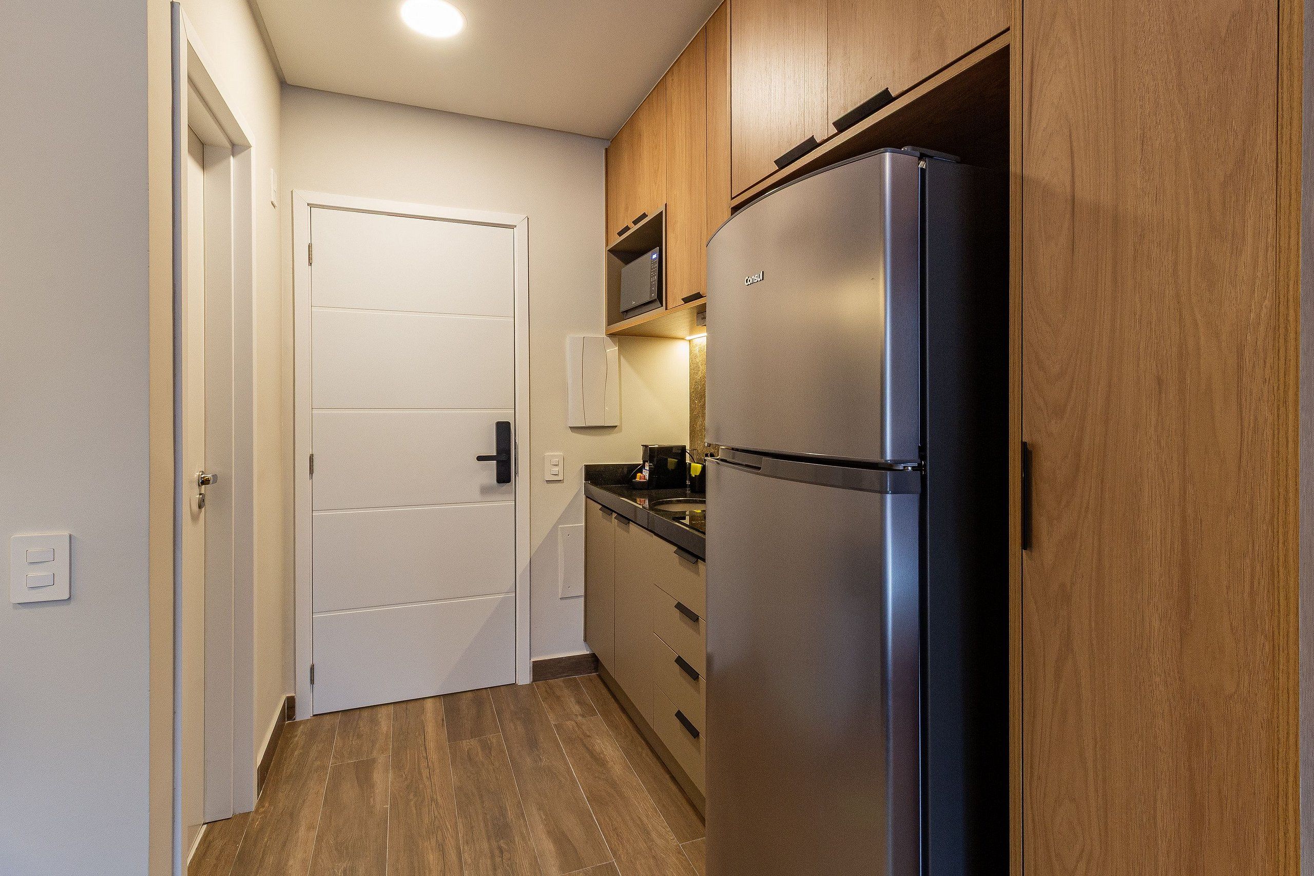 Una cocina compacta con refrigerador empotrado, armarios de madera y microondas.