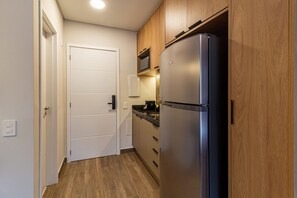 Una cocina compacta con refrigerador empotrado, armarios de madera y microondas.