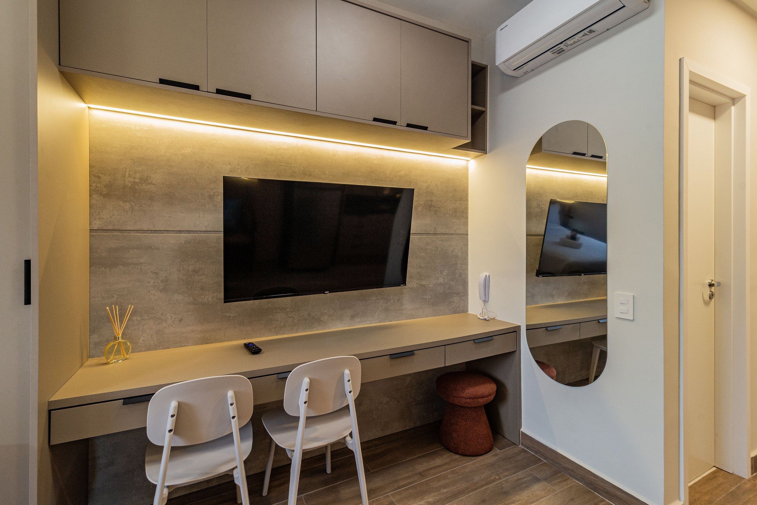 Une chambre moderne avec un téléviseur à écran plat fixé au mur, un petit bureau avec deux chaises et un miroir rond.