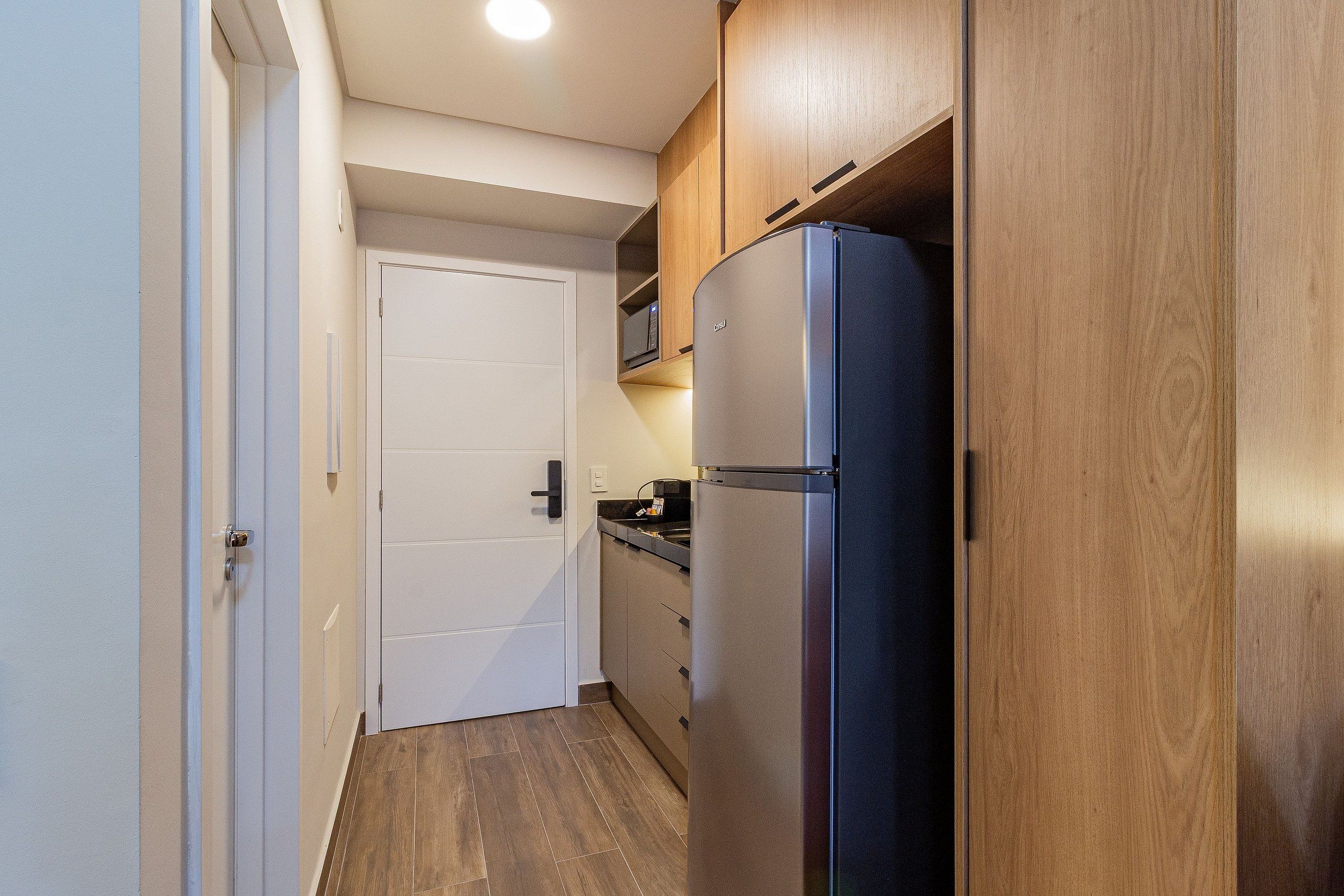 Eine schmale Küche mit Holzschränken, einem Edelstahlkühlschrank und einer weißen Tür.