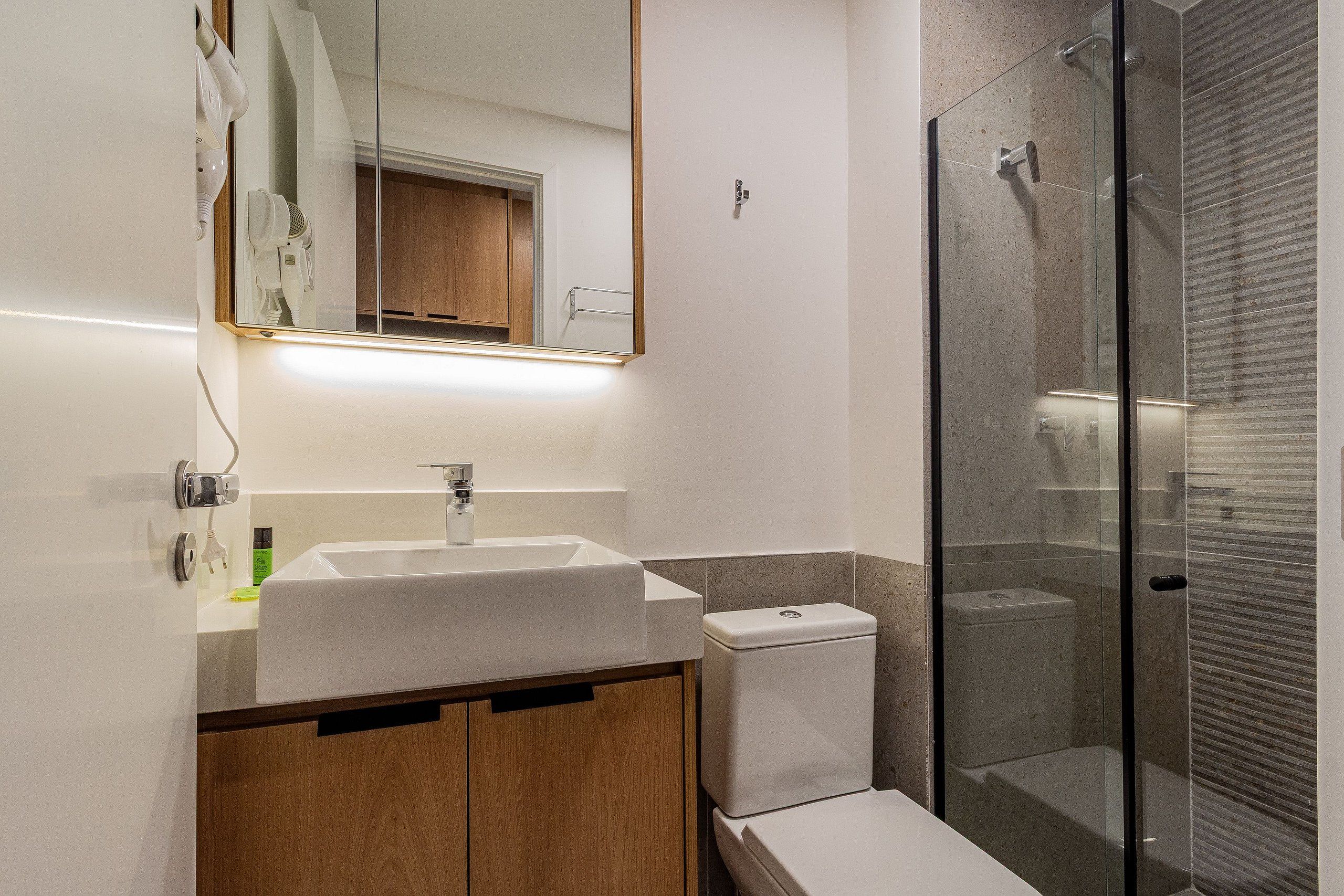 A modern bathroom with a white sink, wooden cabinets, a glass shower enclosure, and a mirror with a wooden frame.