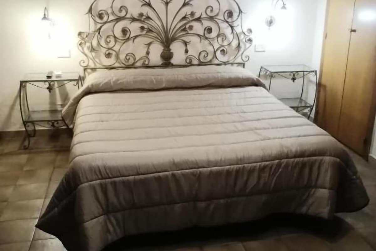 A bedroom with a bed, two bedside tables, a nightstand, a wardrobe, and wall-mounted lamps.
