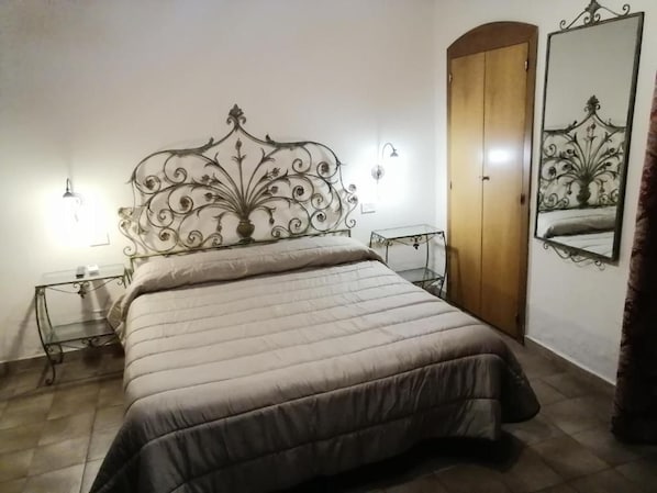 Un dormitorio con una cama, una puerta de madera, un espejo y dos mesitas de noche.