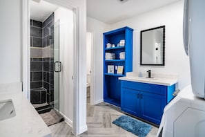 A modern bathroom with a glass shower, blue storage cabinets, and a white sink. - AEA- Crystal Beach (Bolivar Peninsula)