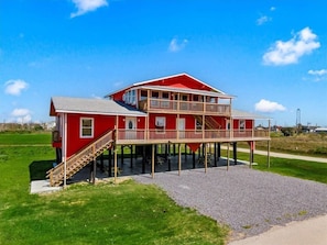 A two-story red house with a balcony, a staircase, and a gravel driveway. - AEA- Crystal Beach (Bolivar Peninsula)
