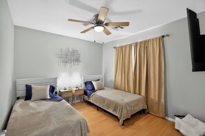 A hotel room with two beds, a ceiling fan, a wall-mounted TV, and a bedside table with a lamp. - 3BR Home Near Las Vegas Strip I Mid-Term Stays (Las Vegas)