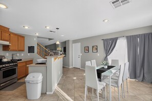 A modern kitchen with wooden cabinets, a gas stove, and a dining area with a glass table and white chairs. - 3BR Home Near Las Vegas Strip I Mid-Term Stays (Las Vegas)