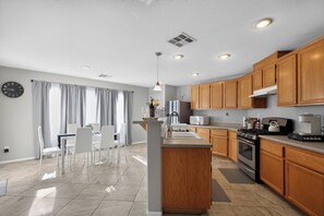 A modern kitchen with wooden cabinets, a central island, and a dining area with white chairs. - 3BR Home Near Las Vegas Strip I Mid-Term Stays (Las Vegas)