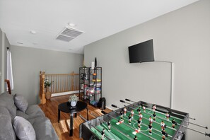 A room with a foosball table, a flat-screen TV, a bookshelf, and a staircase. - 3BR Home Near Las Vegas Strip I Mid-Term Stays (Las Vegas)