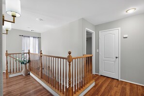 A clean, modern hallway with wooden flooring, a wooden railing, and a white door. - 3BR Home Near Las Vegas Strip I Mid-Term Stays (Las Vegas)