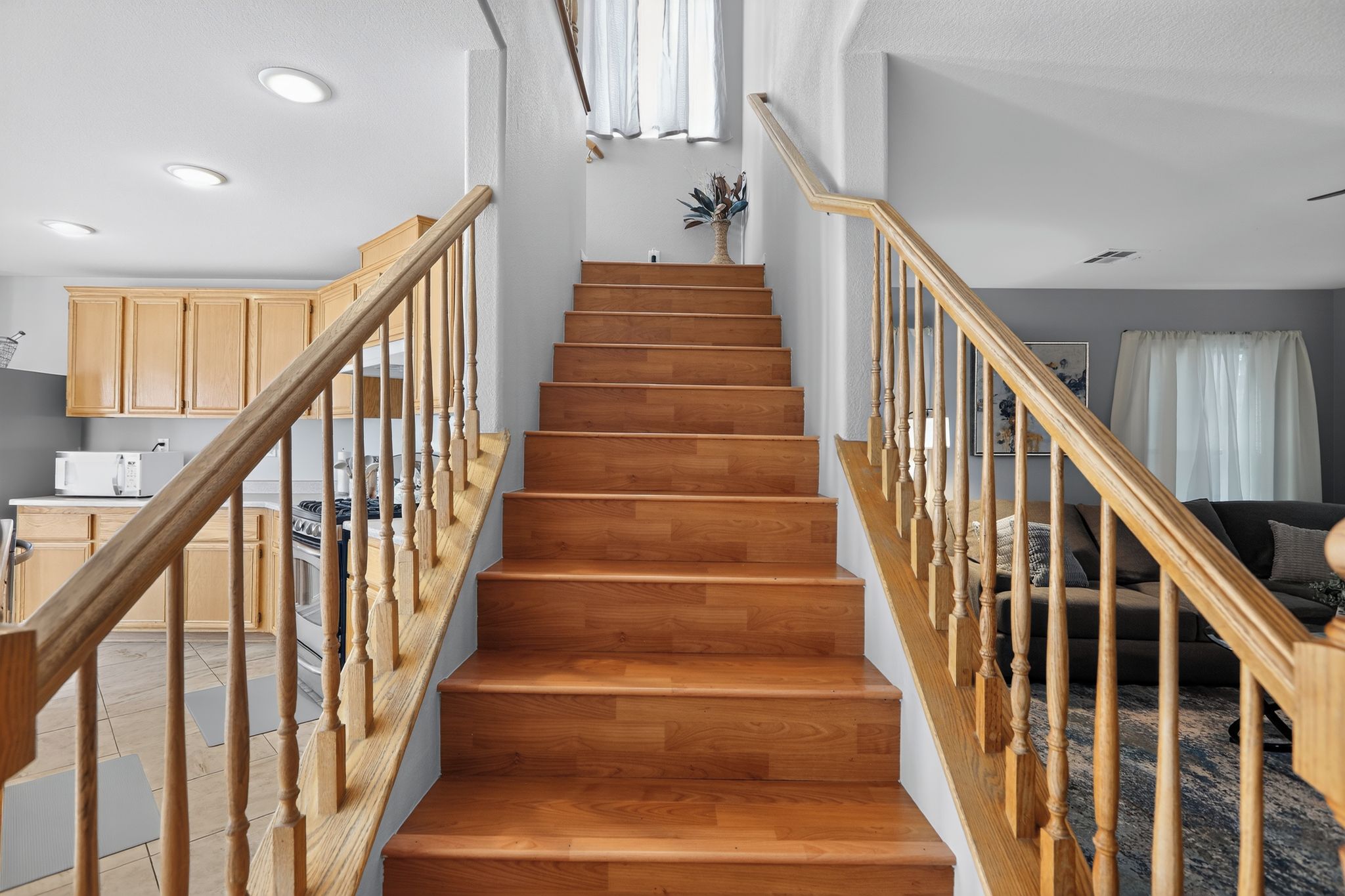 A wooden staircase with a handrail, leading to a landing with a vase of dried plants.