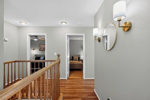 A hallway with a wooden staircase, a bed in the adjacent room, and wall-mounted lighting fixtures. - 3BR Home Near Las Vegas Strip I Mid-Term Stays (Las Vegas)