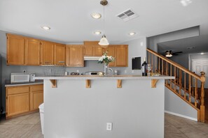 A kitchen with wooden cabinets, a granite countertop, a stainless steel sink, a microwave, and a hanging pendant light. - 3BR Home Near Las Vegas Strip I Mid-Term Stays (Las Vegas)
