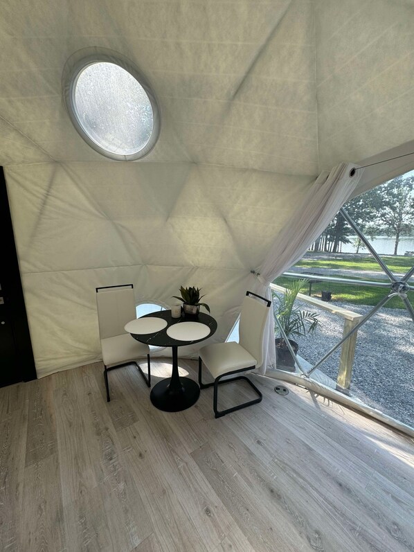 A tent with a round skylight, a table with chairs, and a view of a park.