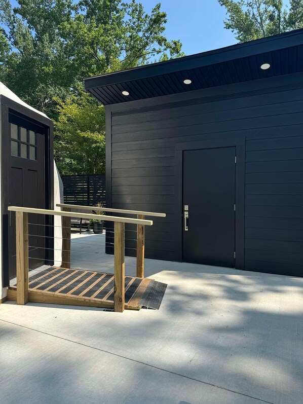 A building with a dark exterior, a door, and a wooden handrail leading to a ramp.