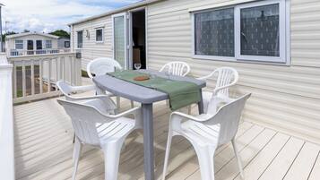 Une maison mobile dotée d’une terrasse, d’une table avec des chaises et d’une fenêtre avec des rideaux.