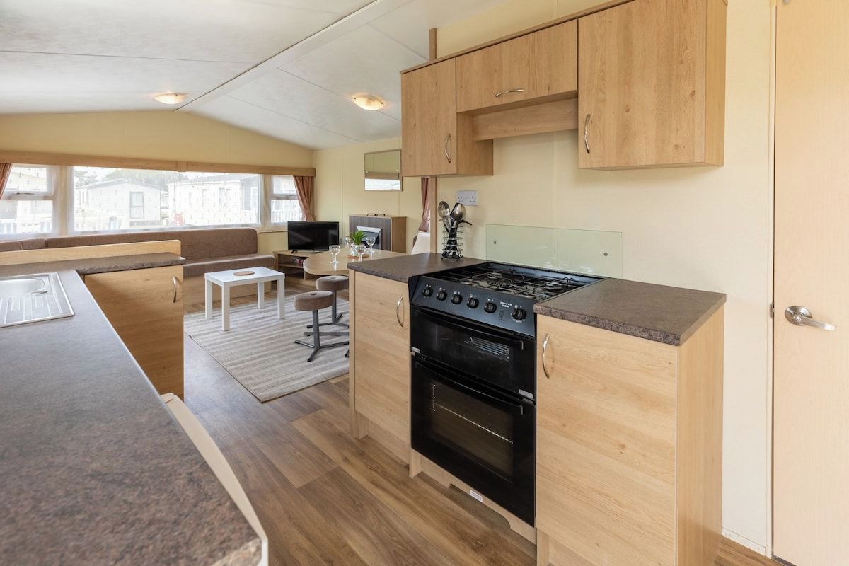 Une cuisine compacte équipée d’une cuisinière, d’un four et de meubles de rangement en bois. On y trouve également un coin repas avec une table et des chaises.
