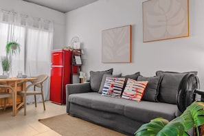 Ein Wohnzimmer mit einem grauen Sofa, einem roten Kühlschrank, einem Esstisch mit Stühlen und einer großen Pflanze.