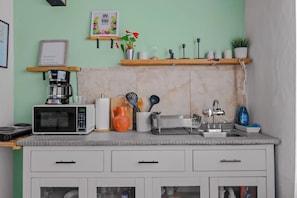 A kitchen with a microwave, toaster, sink, and various utensils. There are shelves with decorative items and a coffee maker. - Casa Esmeralda – Old San Juan (San Juan)
