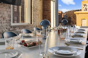 A dining table set with plates, cutlery, and glasses, with a view of a brick building and a yellow building in the background. - Lofted Luxury | 5 BR • Sleeps 10 • Downtown! (Frankfort)