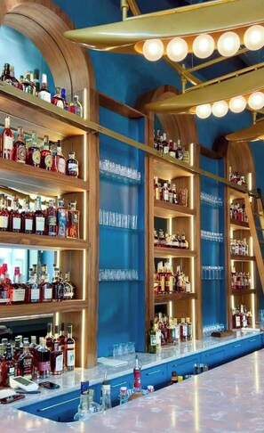 A bar area with shelves of liquor bottles, a bar counter, and a ceiling with lights. - Lofted Luxury | 5 BR • Sleeps 10 • Downtown! (Frankfort)