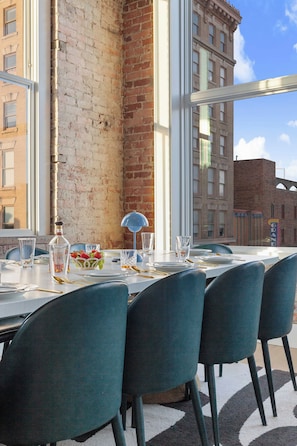An outdoor dining area with brick walls, large windows, and a view of city buildings. - Lofted Luxury | 5 BR • Sleeps 10 • Downtown! (Frankfort)